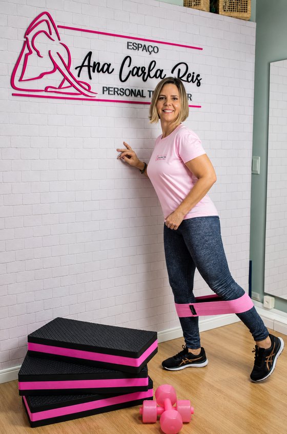 Ana Carla Reis em pé ao lado do letreiro do estúdio, pronta para orientar um treino